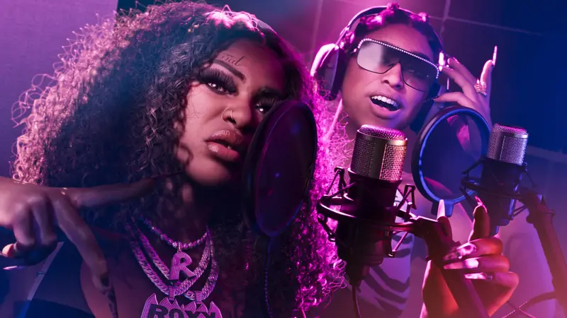 Two artists recording in a purple-lit studio booth